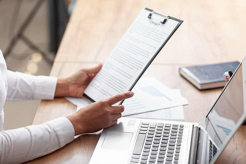 Businesswoman reviewing contract clipboard laptop desk