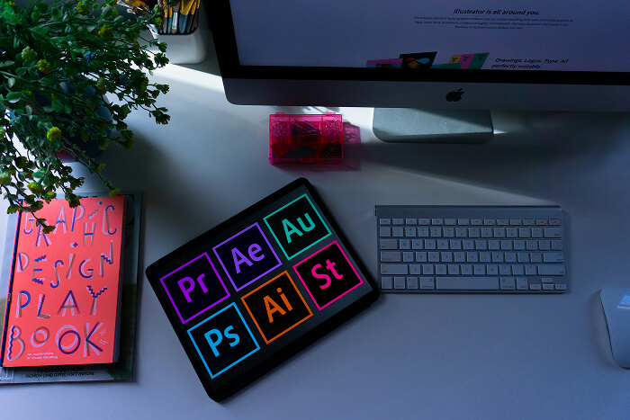 Creative desk setup with Adobe Creative Cloud apps on a tablet, design books, and a computer screen in a modern workspace.